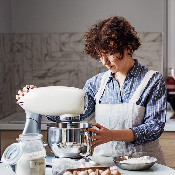 Een dame bereidt een cake met een witte keukenmachine in haar keuken