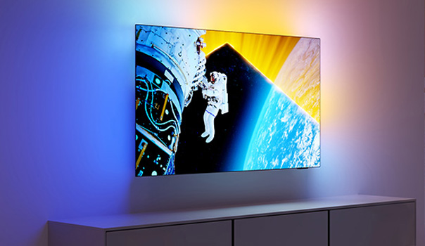 Een televisie dat aan de muur hangt en waarbij de kleuren rond het scherm geprojecteerd worden