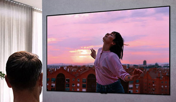 Een man kijkt naar de tv met op het scherm een dansende vrouw tijdens de zonsondergang